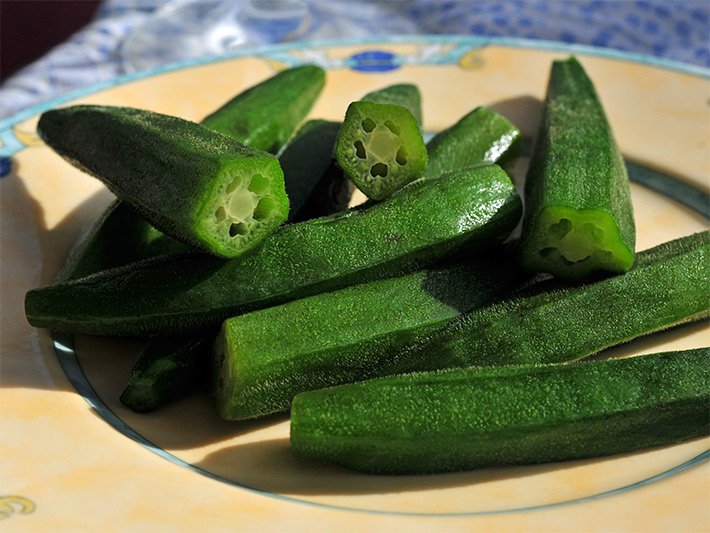 Mehrere gekochte, ganze und aufgeschnittene grüne Okra-Pflanzen, auch Okraschoten, auf einem Porzellanteller in der Küche