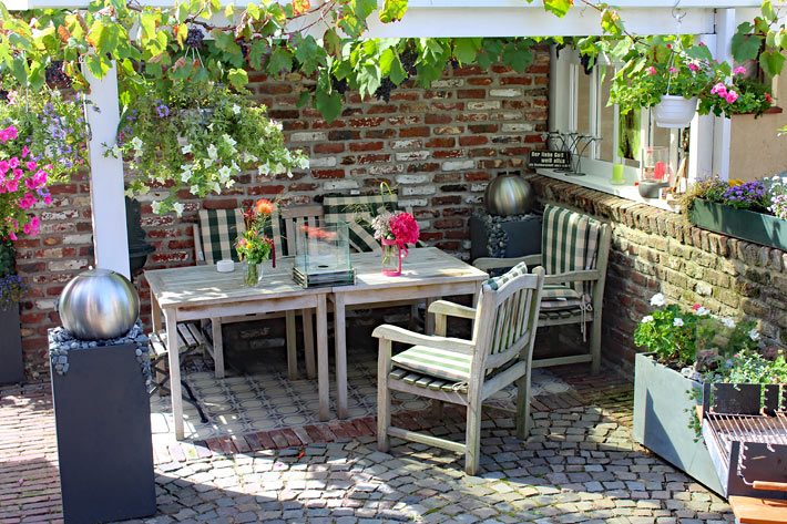 Terrasse mit Holztisch und Stühlen, dekoriert mit verschiedenen Blumen-Töpfen