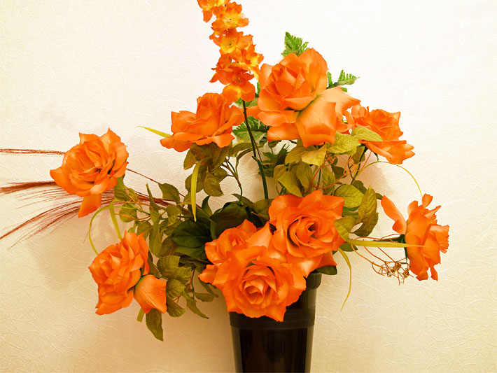 Schwarze Vase mit orangen Rosen und Deko-Beiwerk wie braune Gräser und grüne Blätter