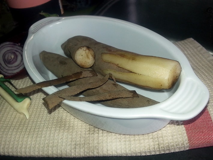 Grau-braune Yacon-Gemüse-Knolle geschält und aufgeschnitten sowie als ganzes Stück auf einem weissen Teller