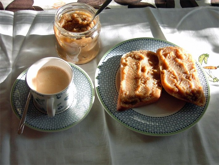 Frühstücks-Rezept für gold-braune Yacon-Marmelade auf zwei Butter-Brötchen mit einer Tasse Kaffee und dahinter ein geöffnetes Glas gefüllt mit Yaconmarmelade