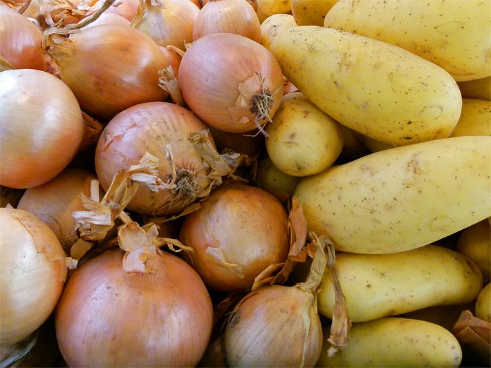 Zwei getrennte Haufen ungeschälter Zwiebeln und Kartoffeln nach dem Ernten zusammen lagern