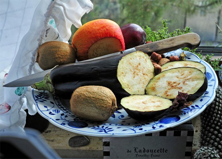 Aufgeschnittene, dunkel-violette Aubergine auf einem Porzellanteller zum Zubereiten mit Auberginen-Scheiben