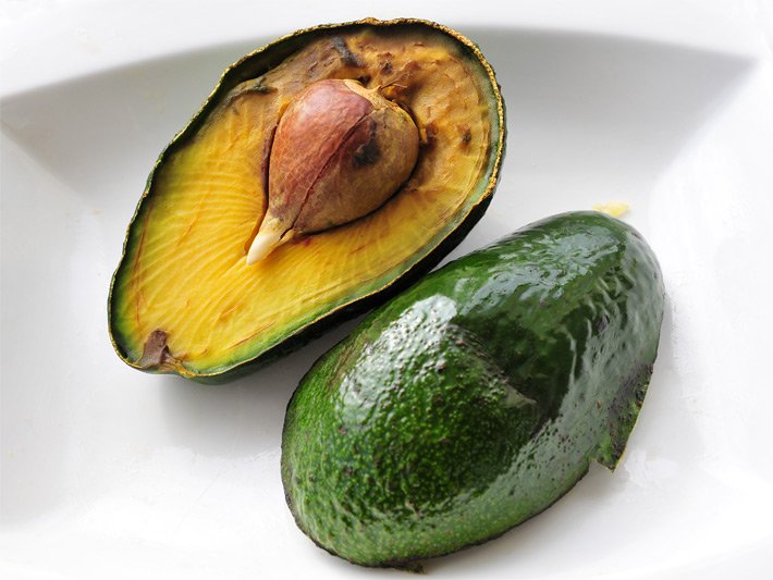 Zwei Hälften einer aufgeschnittenen Avocado-Pflanze der Sorte Fuerte mit dunkelgrüner, glänzender Rückseite und Innenseite mit hellbraunem Kern und gold-gelbem Fruchtfleisch