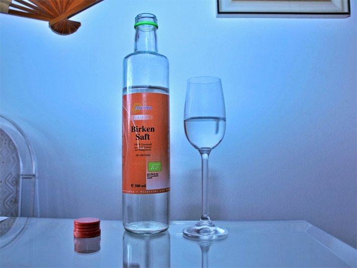 500 ml Flasche Bio-Birkensaft-Anwendung von Aurica und ein halb eingeschenktes frisches Glas mit wässrig durchsichtiger Farbe und Konsistenz, 100 % Direktsaft aus dem Stamm der Hängebirke nach DE-ÖKO-001