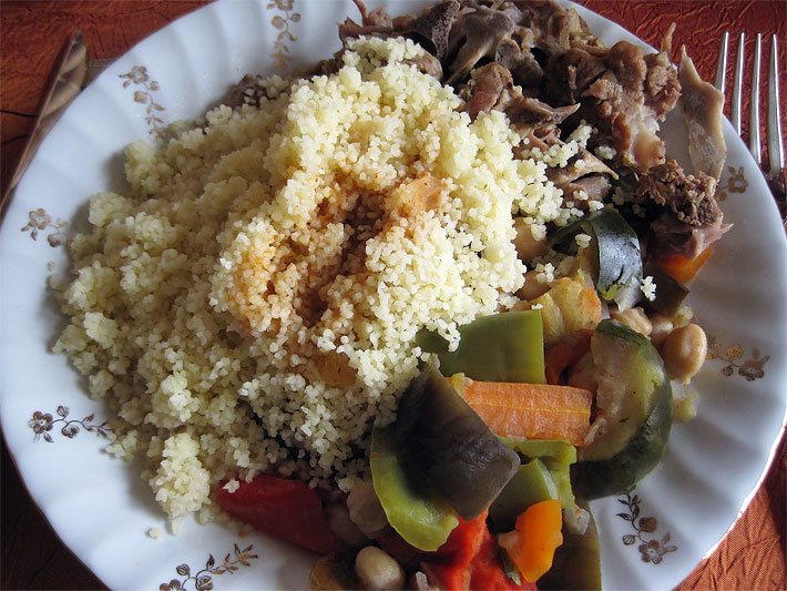 Ein weißter Teller Couscous mit Fleisch und gekochten Zucchini, Tomaten, Bohnen und Karotten