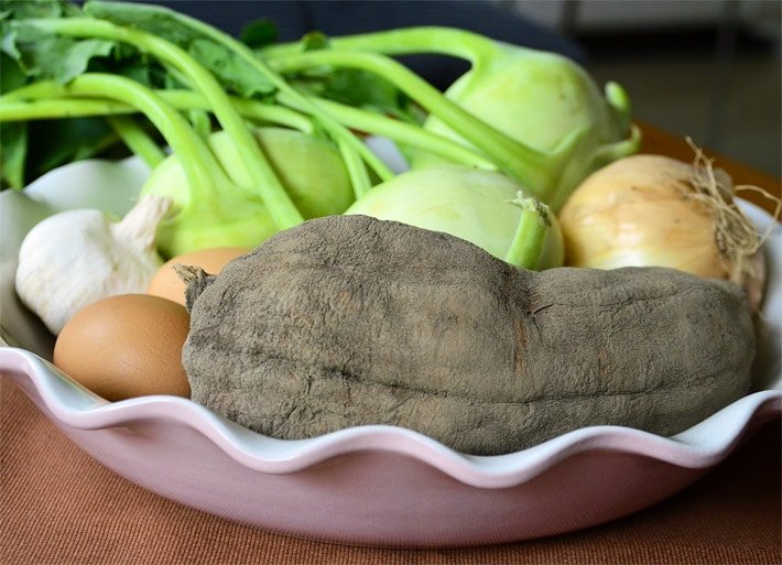 Weiße Porzellan-Schale mit Eiern, Zwiebeln, Knoblauch- und Kohlrabi-Knollen sowie einer reifen grau-braunen Yacon-Knolle