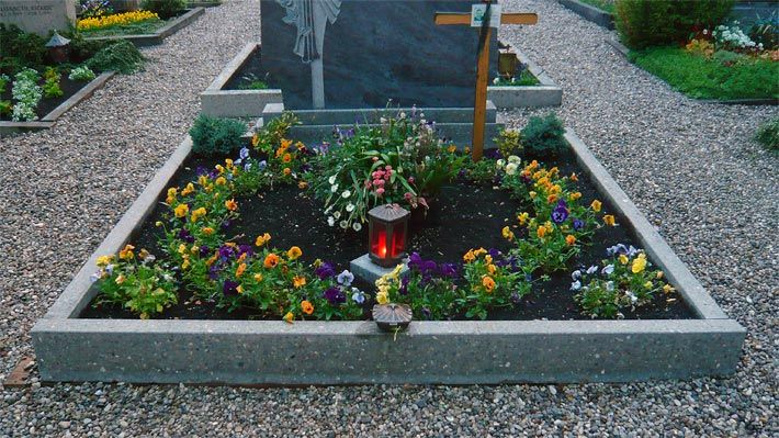 Friedhofsblumen auf einem Grab mit Grabkerzen-Lampe