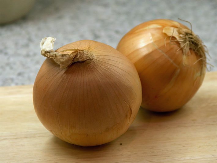 Ungeschälte, dunkel-gelbe Küchen-Zwiebeln auf einem Holzbrett