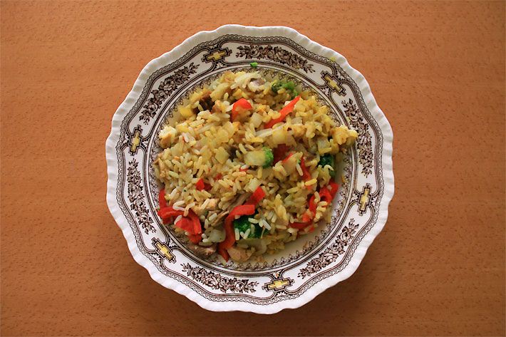 Porzellan-Teller mit gebratener Gemüsereispfanne bestehend aus Brokkoli, rotem Paprika und Zwiebeln