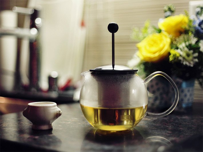 Teekanne aus Glas zur Hälfte gefüllt mit grünem Tee