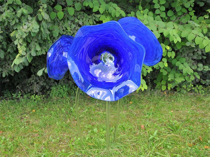 Drei handgeformte, gläserne blaue Blumen auf durchsichtigen, über 50 cm hohen Stiehlen als Gartendekoration