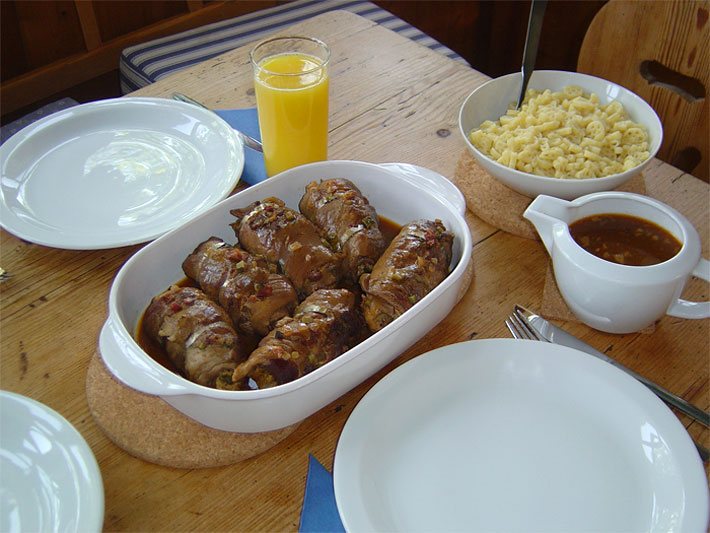 Gedeckter Holz-Esstisch vor Essbeginn mit Rouladen, brauner Soße und Cavatappi-Pasta aus Hartweizen in weißen Porzellan-Service