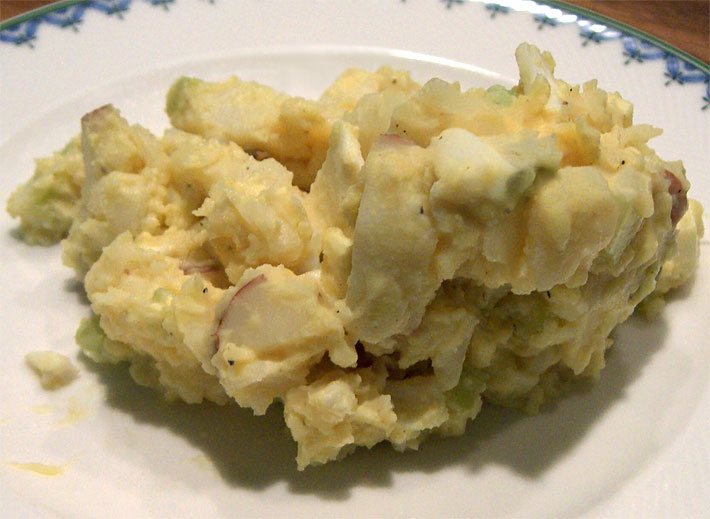 Ein weißer Teller mit Kartoffelsalat aus gekochten Kartoffeln angemacht mit Zwiebeln