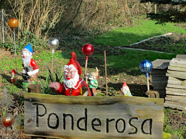 Klassische Gartenzwerge zusammen mit Deko-Glaskugeln zur Gartendekoration in einem Garten mit einem Holzschild der Ponderosa-Ranch in der Fernsehserie Bonanza