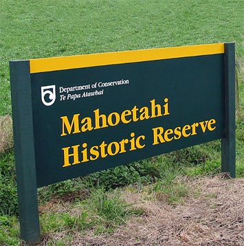 Koru-Symbol eines eingerollten Farns im Logo vom Department of Conservation (DOC) auf einem Schild des nationalen Schutzgebietes Mahoetahi Historic Reserve in der Nähe der Stadt Waitara in der Region Taranaki auf der Nordinsel von Neuseeland