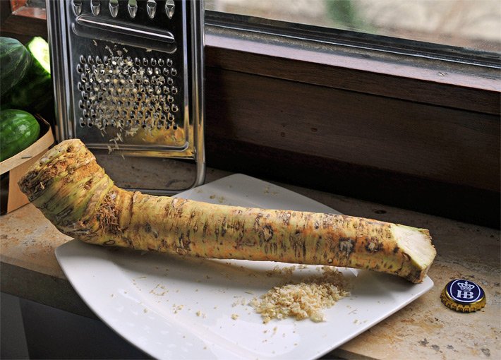 Meerrettich-Knolle auf einem weißen Teller mit Gemüseraspel und geraspeltem, weißem Kren auf dem Küchen-Fensterbrett