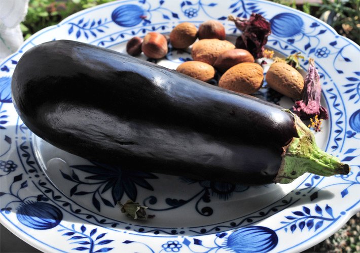 Melanzani oder Aubergine in dunkelvioletter Farbe auf einem Porzellanteller mit Nüssen