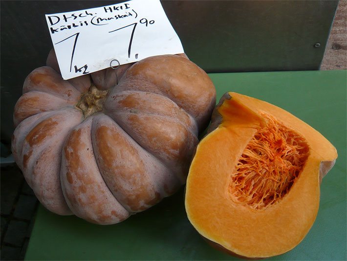 Ein ganzer, brauner Muskatkürbis und ein aufgeschnittener mit orangem Fruchtfleisch