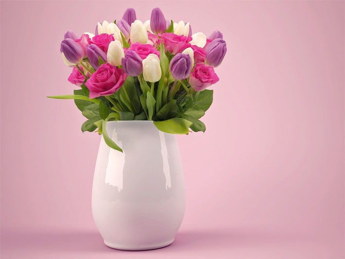 Weiße Porzellan-Vase mit Schnittblumen bestehend aus roten Rosen sowie weißen und purpurfarbenen Tulpen