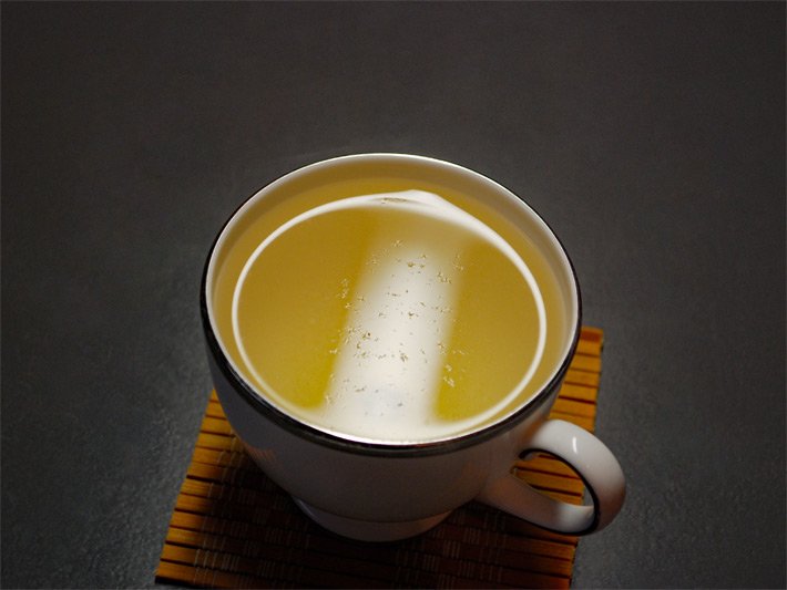 Eine Tasse gefüllt mit hellem Weißhaar-Silbernadeltee, auch Bai Hao Yin Zhen oder Baihao Yinzhen, mit den feinen abgelösten Härchen der Blattknospen