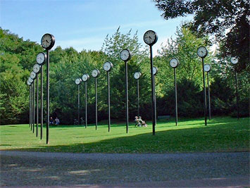 Das Zeitfeld im Südpark Düsseldorf vom Künstler Klaus Rinke, ein Wiese mit geometrisch aufgestellten Bahnhofs-Uhren auf Laternenmasten