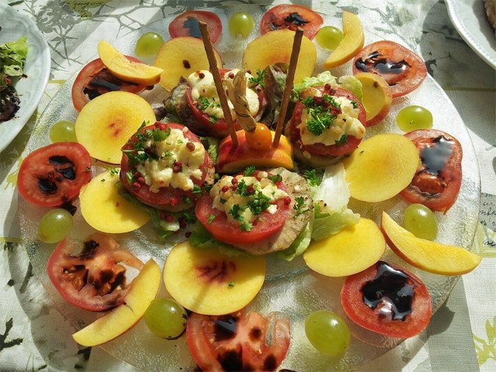 Rezept-Idee für gemischtes Obst und Fruchtgemüse mit Yacon-Wurzelscheiben, rohen Tomaten-, Pfirsich- und Apfel-Scheiben und Weintrauben, garniert mit Kräutern, Schafskäse und Dressing